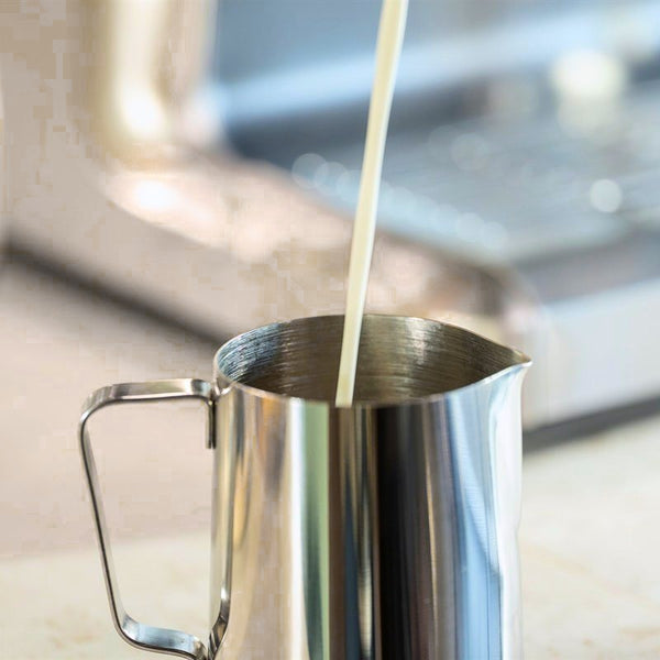 Milch wird in ein Milchkännchen aus Stahl gegossen