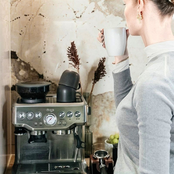 Eine Frau trinkt Kaffee an ihrer Espressomaschine