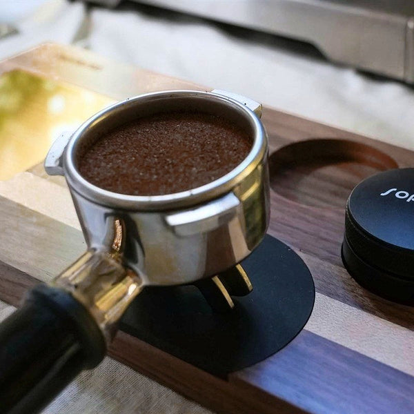 Ein Siebträger mit Kaffee neben einer Sopresta-Tampermatte